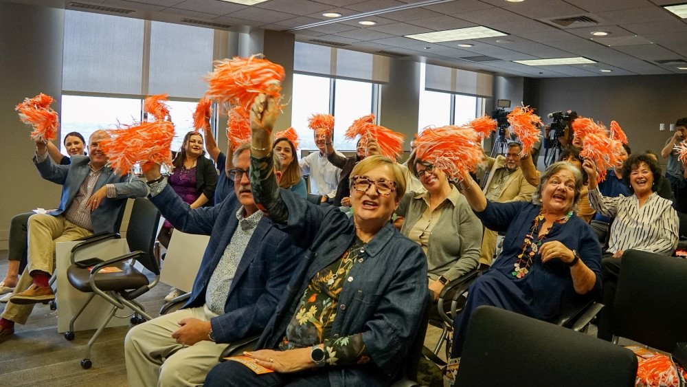 A large group of people seated and waving pom-poms. 