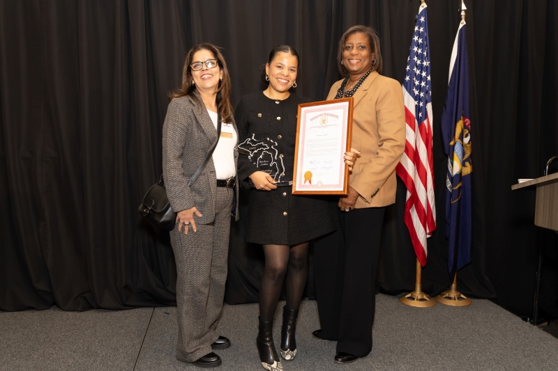 Three people standing together with the person in the middle holding two awards.