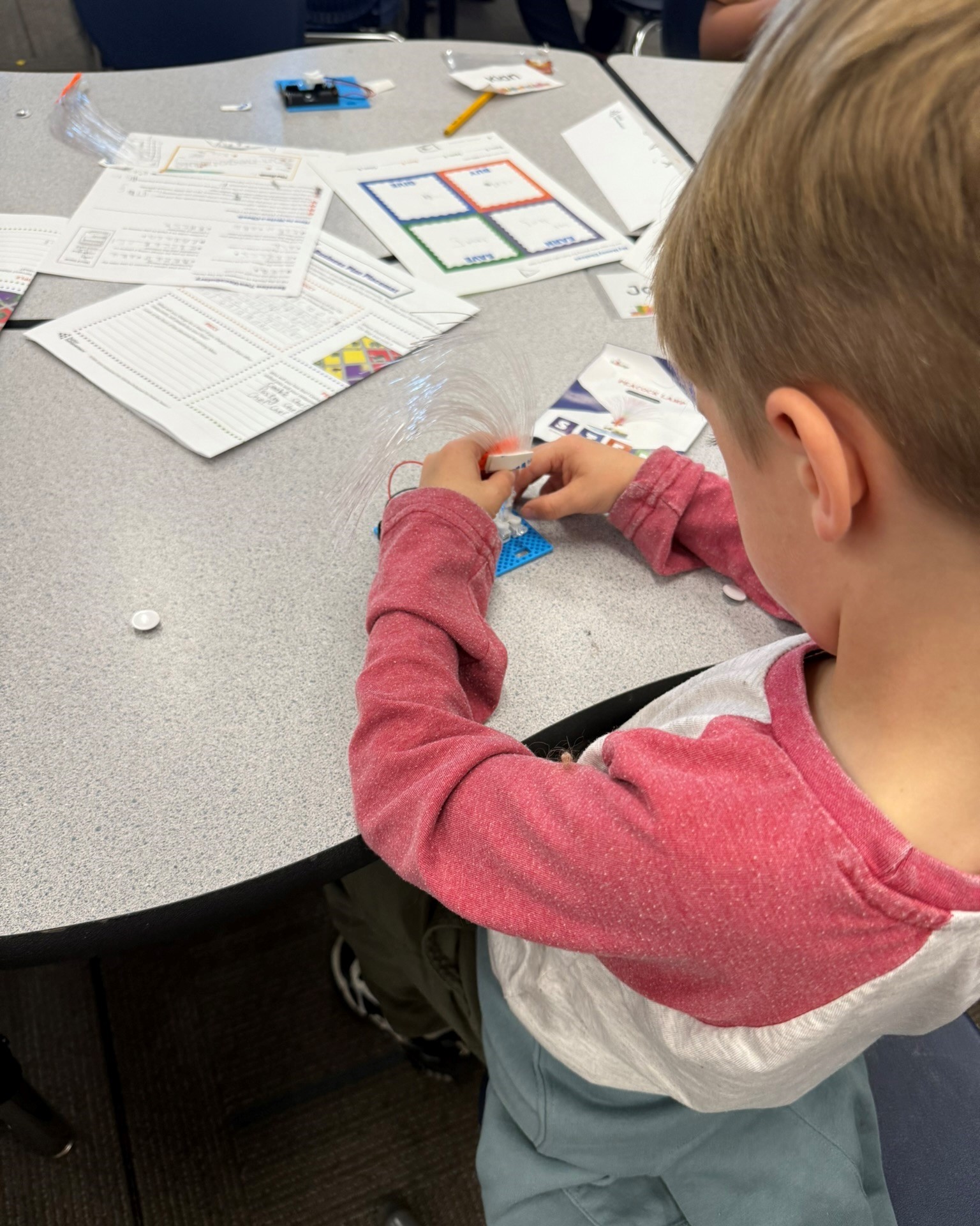 A child at a desk holds parts to object to be put together.