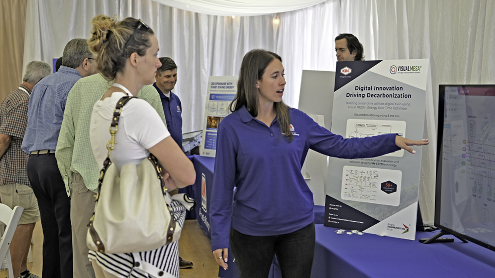 A woman points to a tv screen on a table in conversation with another woman.
