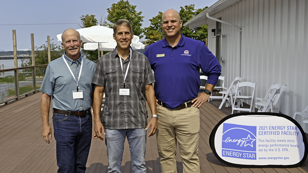 Three men stand together outside with an ENERGY STAR displayed behind them.