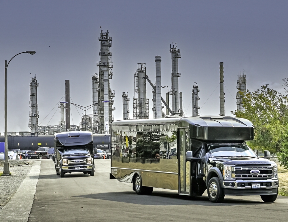 Two tour buses drive in front of the Anacortes refinery.