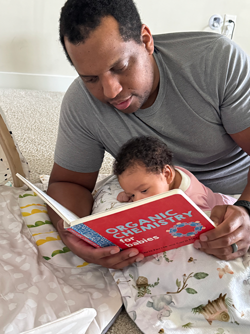 An adult reading a book to a baby while sitting together.