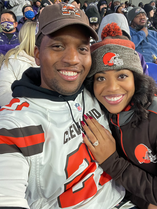  Two people posing for a photo at a football stadium with fans behind them.