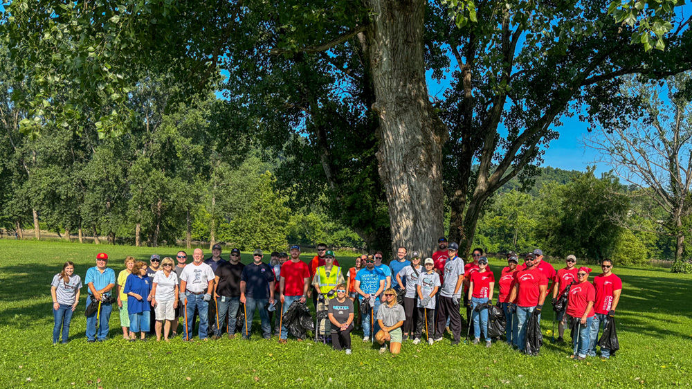 A large group of people gathered on the grass in front of a big tree.