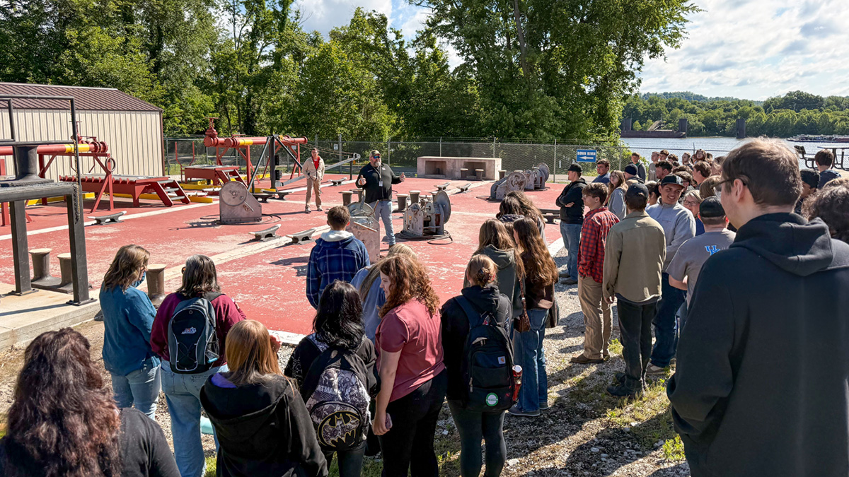 Students watch a demonstration at a training pad outside next to a river.
