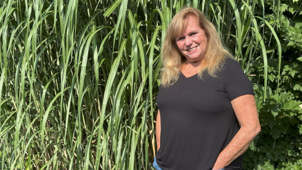 Linda Vandeneynde stands in front of green landscape.