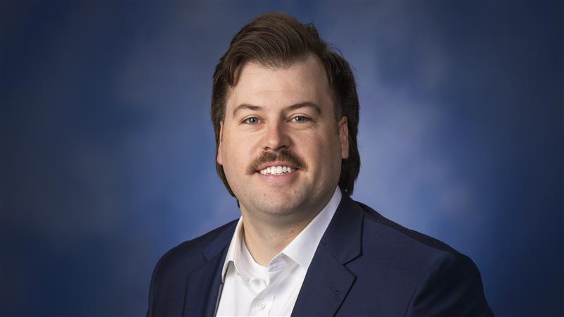 Portrait of Zach Dollich against a blue background.