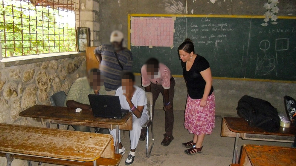 Five people looking at a laptop in a classroom.