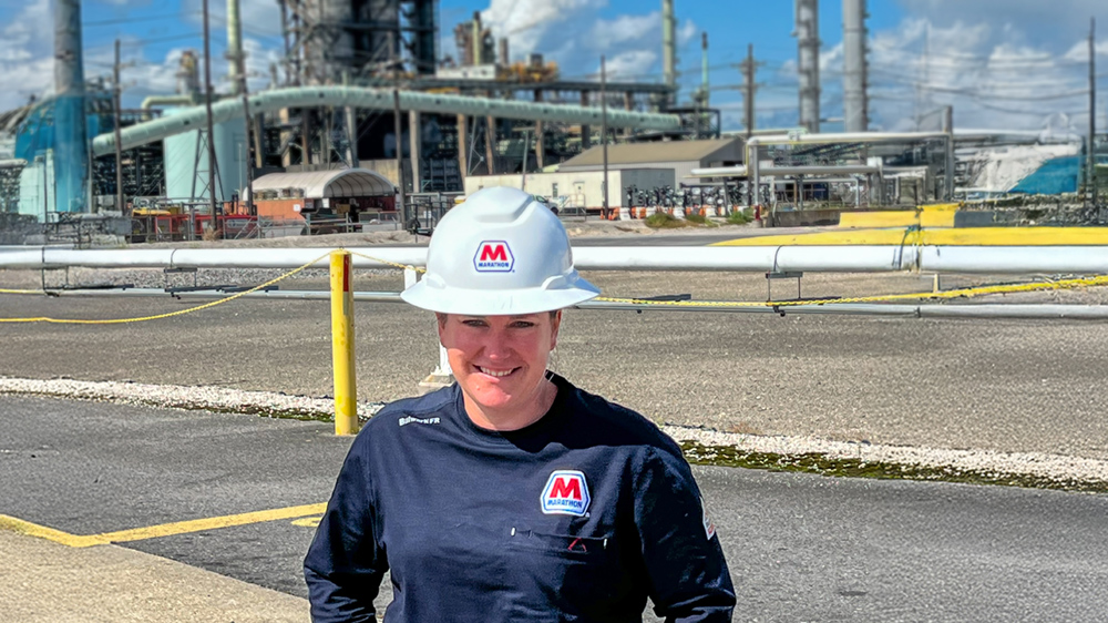 A young woman wearing safety gear is standing and smiling with her hands in her pockets.