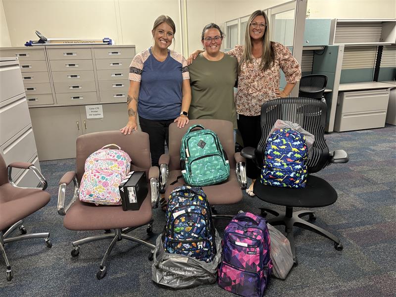 Three people standing by chairs with backpacks in them. Three people standing by chairs with backpacks in them.