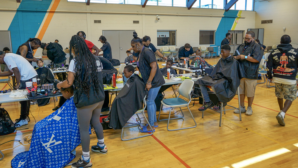Children getting haircuts from stylists in a gym. Children getting haircuts from stylists in a gym.