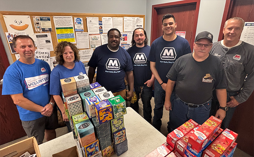 A large group of people pose for a photo with backpacks and boxes of items. A large group of people pose for a photo with backpacks and boxes of items.
