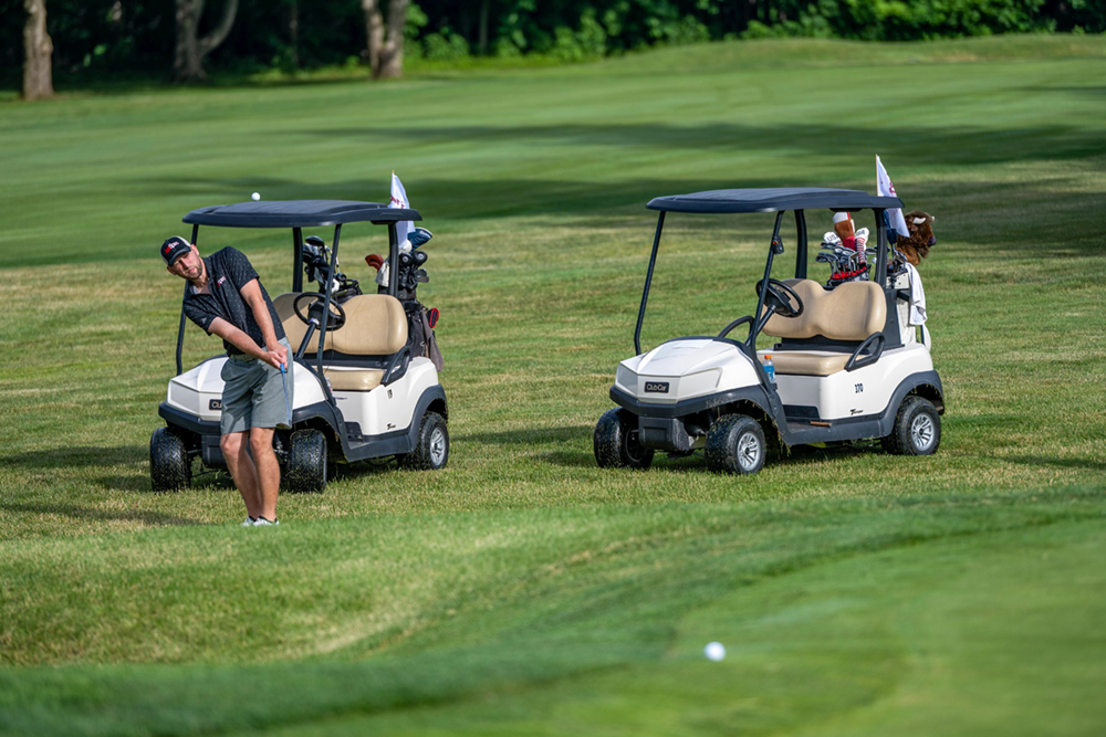 A golfer hits a ball in front of two golf carts.