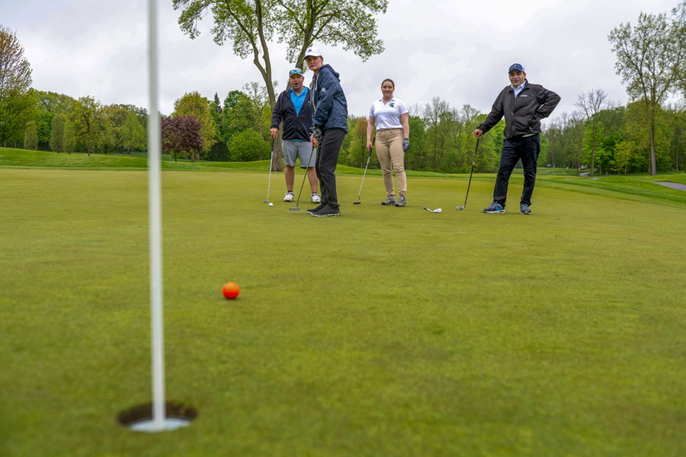A golfer watches a golf ball roll toward the hole.