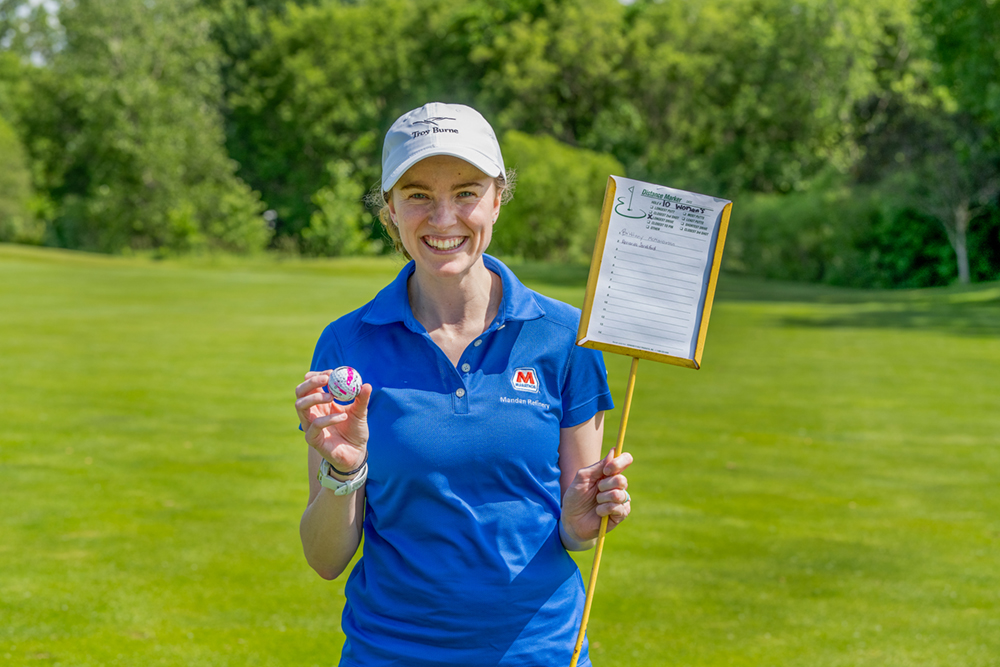 : A woman holds a sign and a golf ball on a golf course.
