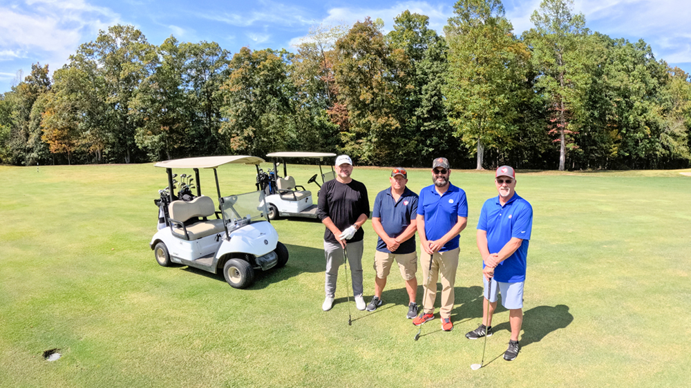 Four golfers standing on a golf course by two golf carts.
