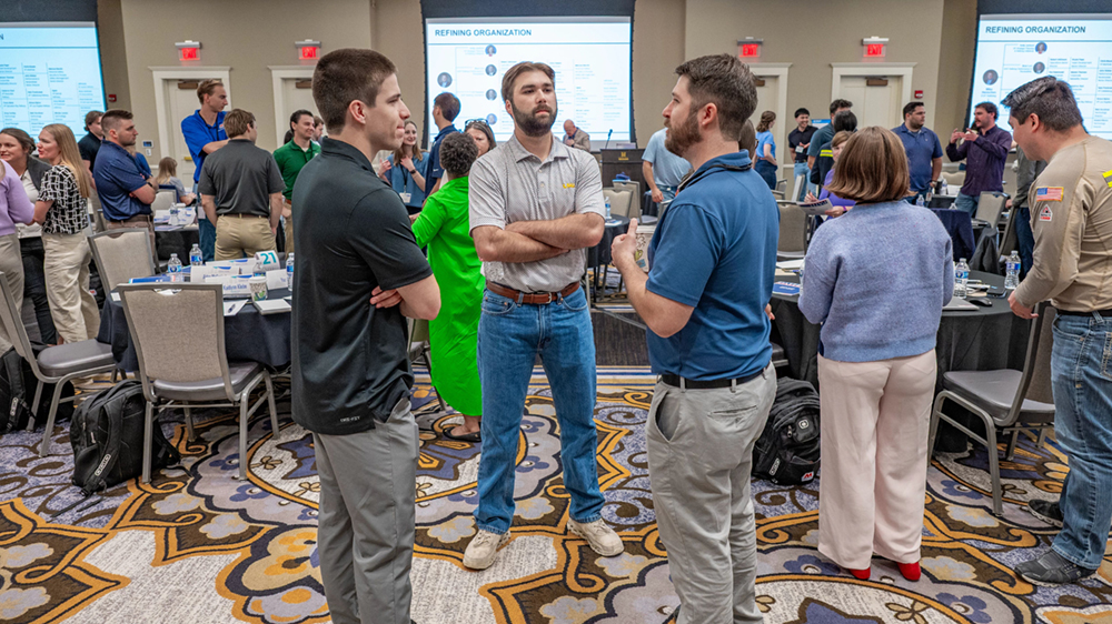 Three people engaged in a conversation with others around them in the conference room.