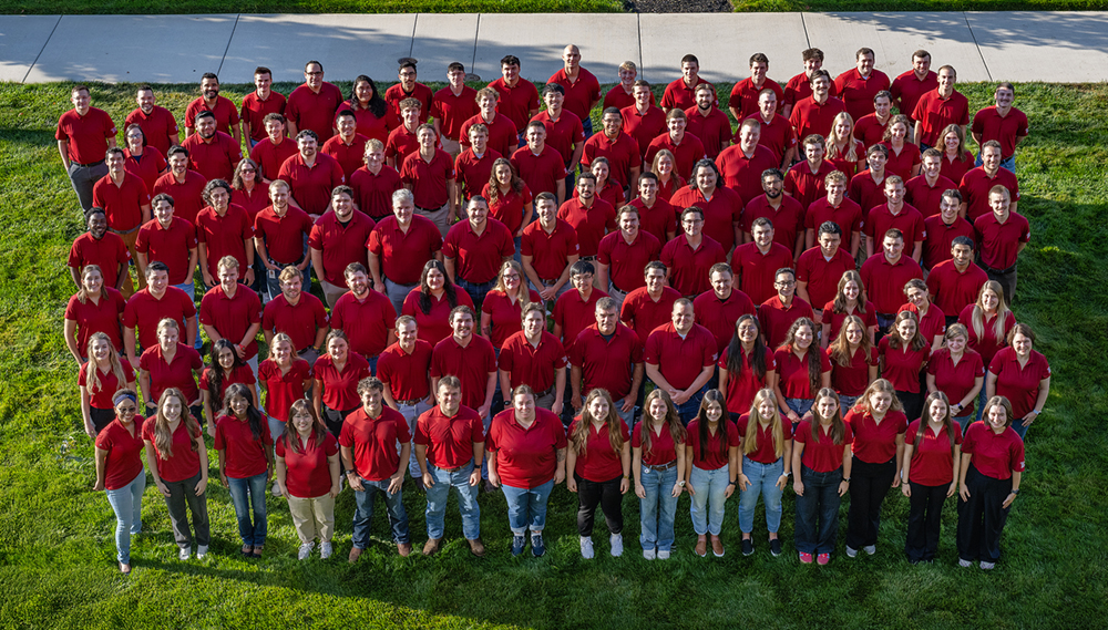 An aerial view of a large group of people wearing red shirts standing on a green lawn.