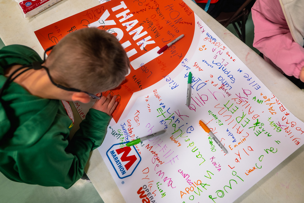 A child signs a banner on a table indoors.