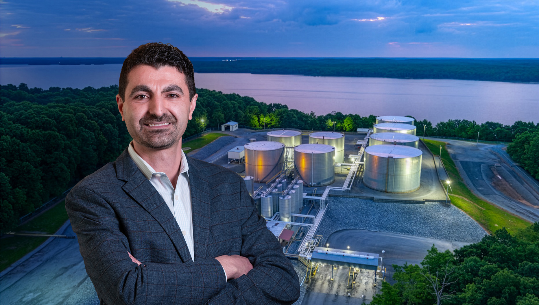 A man standing in front of an Aerial view of an asphalt terminal by a body of water in the background.