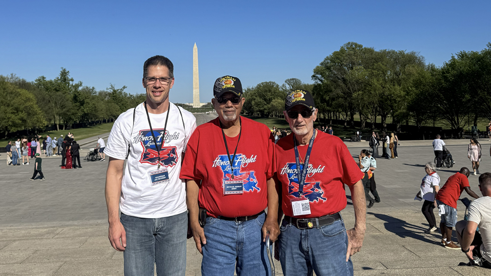 Three people standing together outdoors with the Washington Monument in the background.