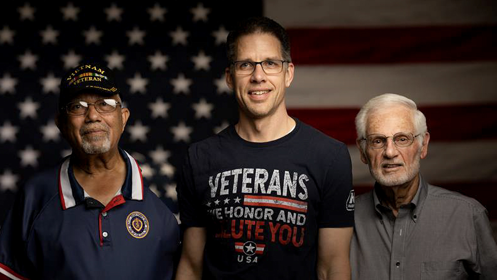 Three men standing together for a photo with an American flag in the background.