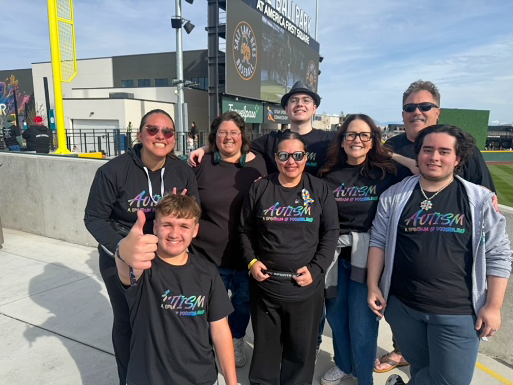 A group of people standing in rows with a baseball field behind them. 