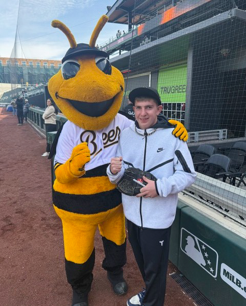 A boy stands next to a costumed team mascot of a Bee.