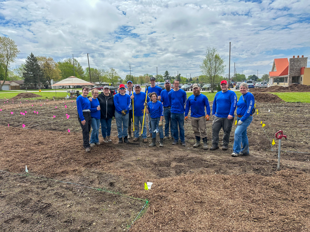 Volunteers pose with shovels, rakes and other gardening tools during a community service project.