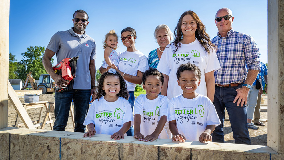 A group of people stands together at a construction site where a new home is being built.