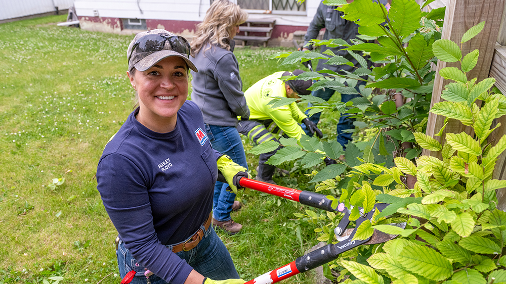 A woman holds a garden tool in her hand while trimming greenery.