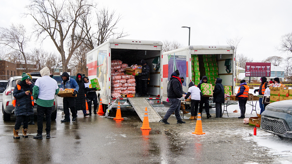 People unload food boxes from box trucks in a parking lot. 