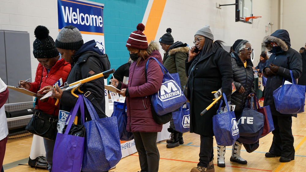 A group of people standing in line and holding bags of winter weather gear.