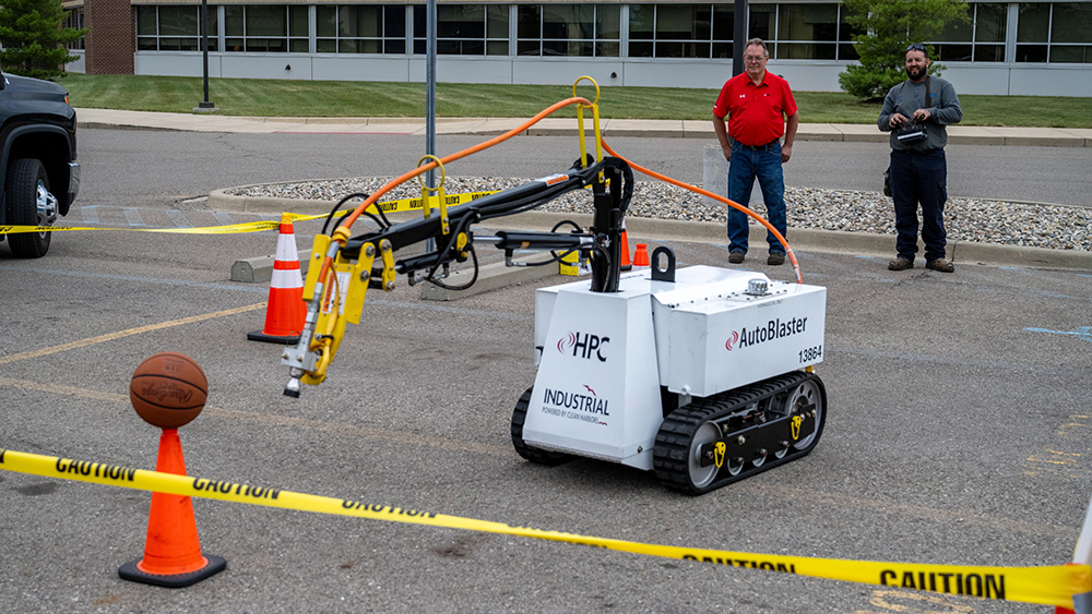 A machine moves toward a basketball balanced on a safety cone. 