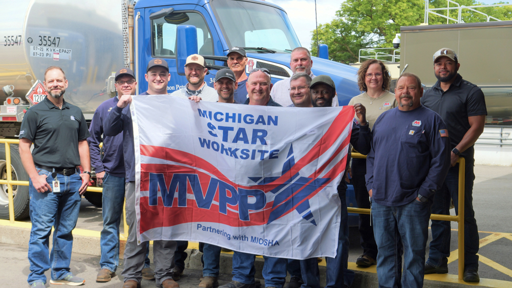 : A group of employees stand together holding a flag that says Michigan STAR Worksite MVPP.