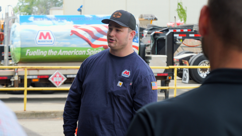 A man in a blue work shirt speaks in front of people.