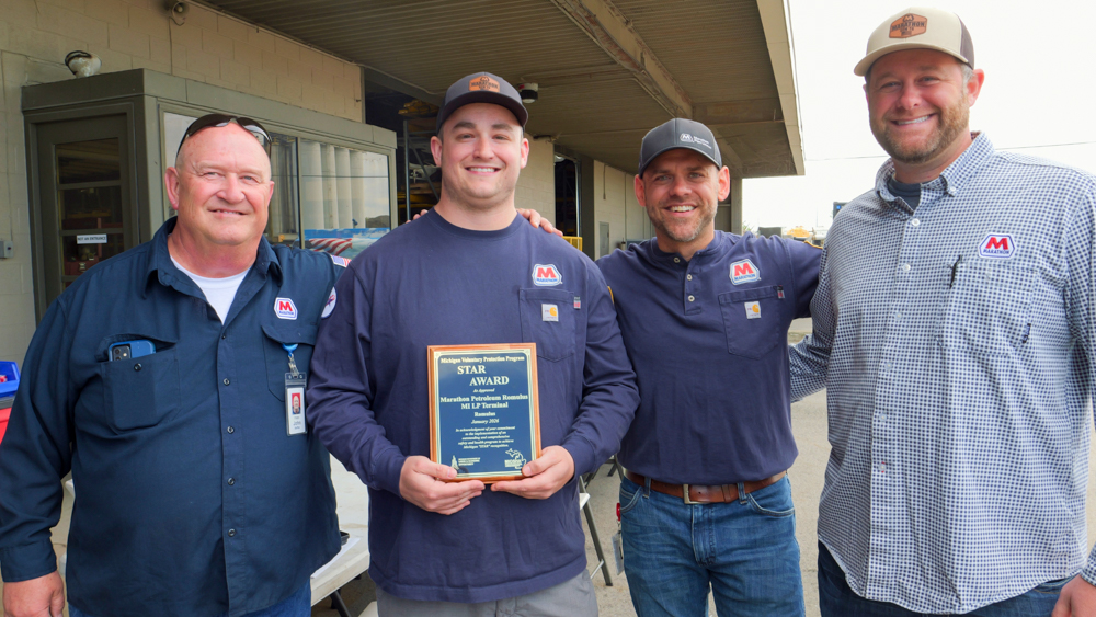 Four men stand together holding a plaque from MIOSHA.