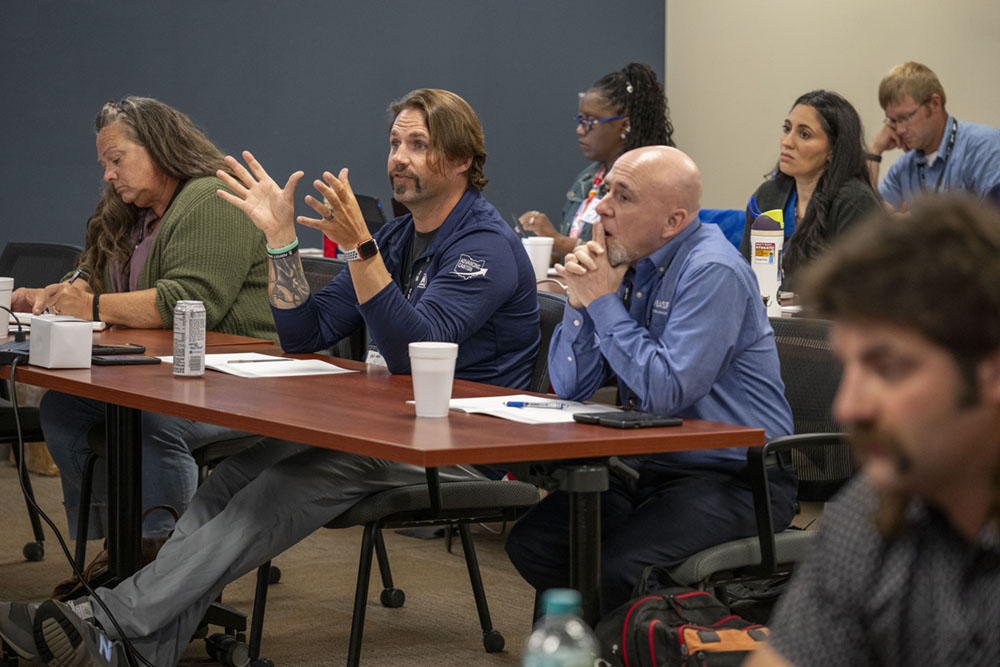 A man sitting at a table near others in a classroom.