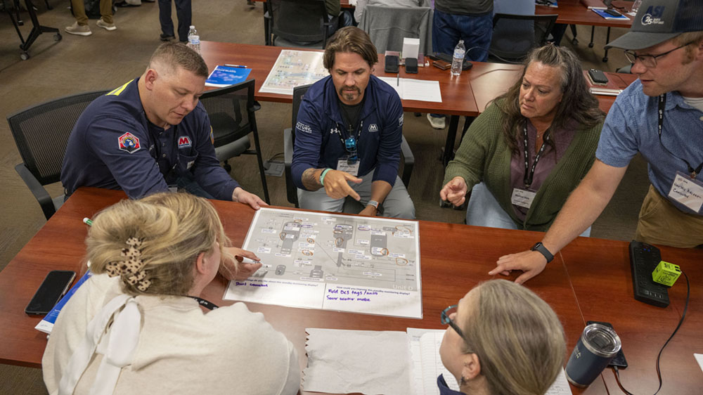 A group of people sit around a table and look at a process control overview document.