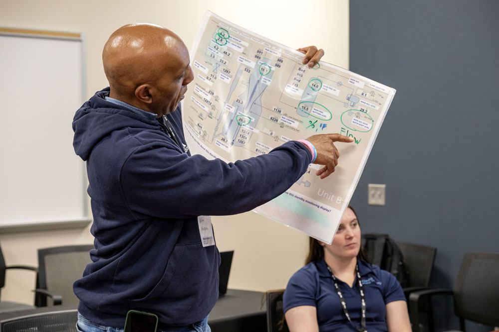 A man holds a process control overview document and points to a section. 