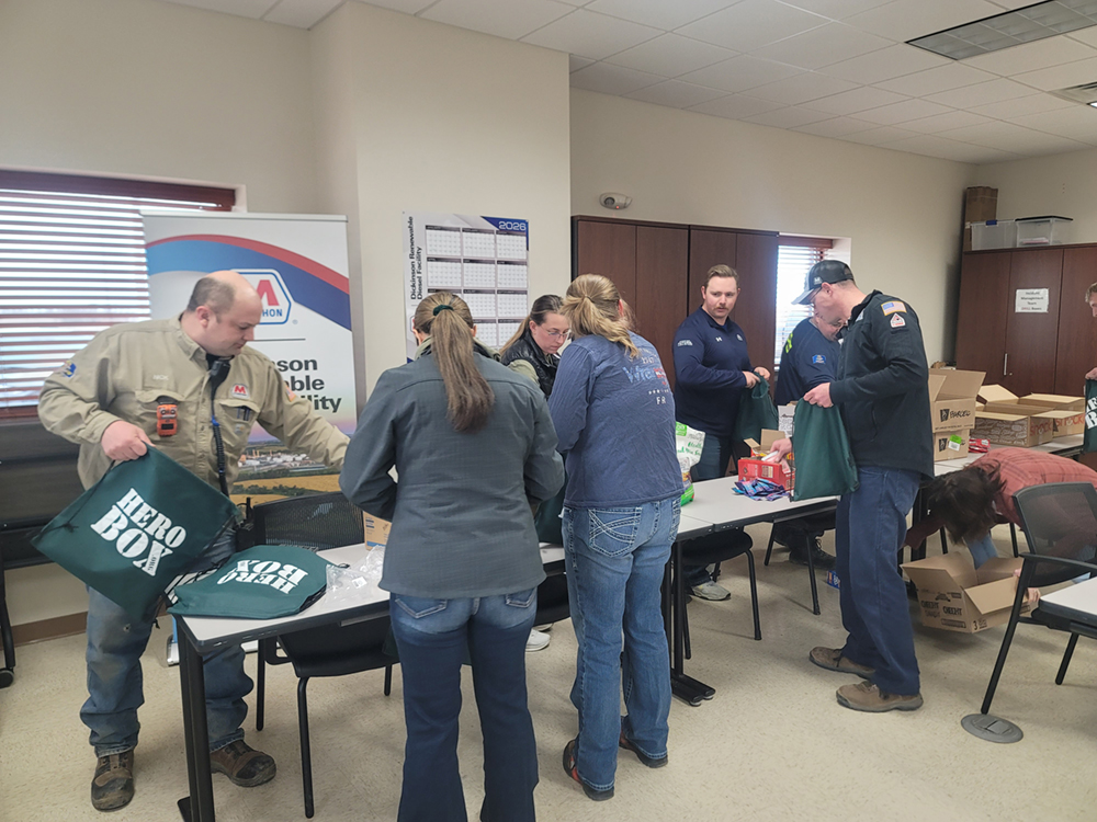 People stand around a table, placing assorted supplies into bags during a care package packing event.