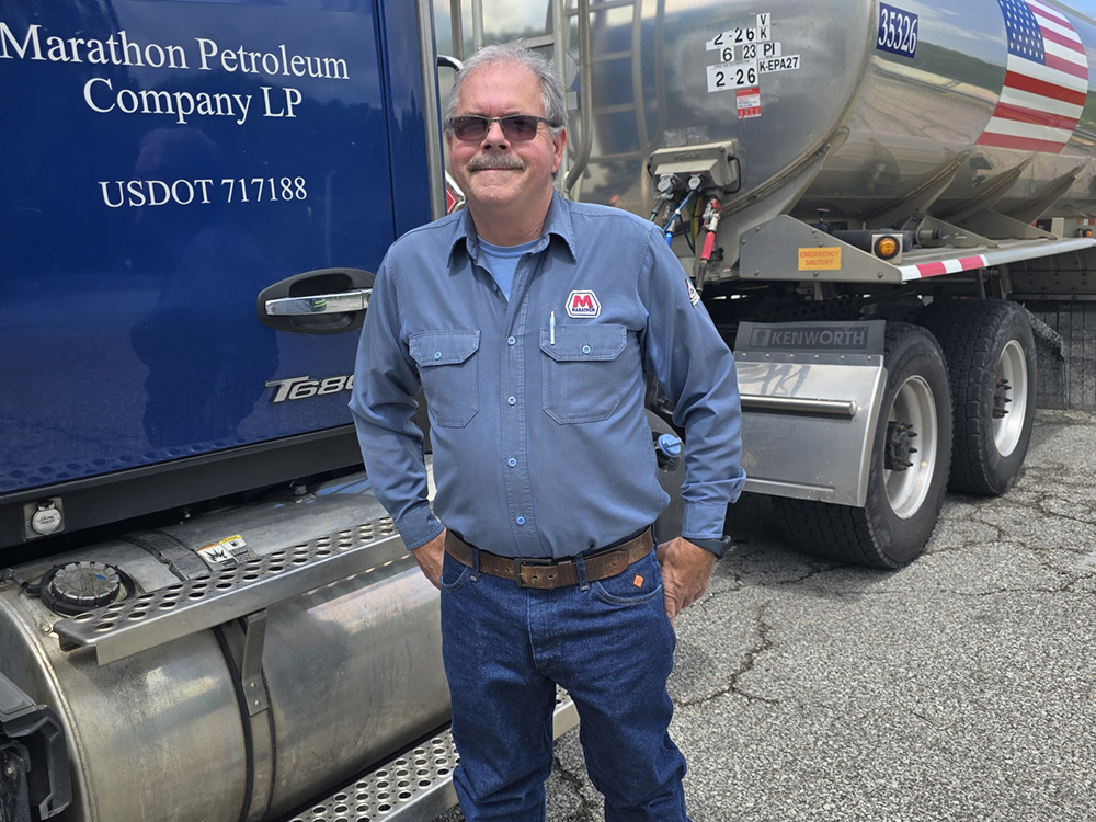Man wearing a blue Marathon shirt stands by his tractor trailer. 