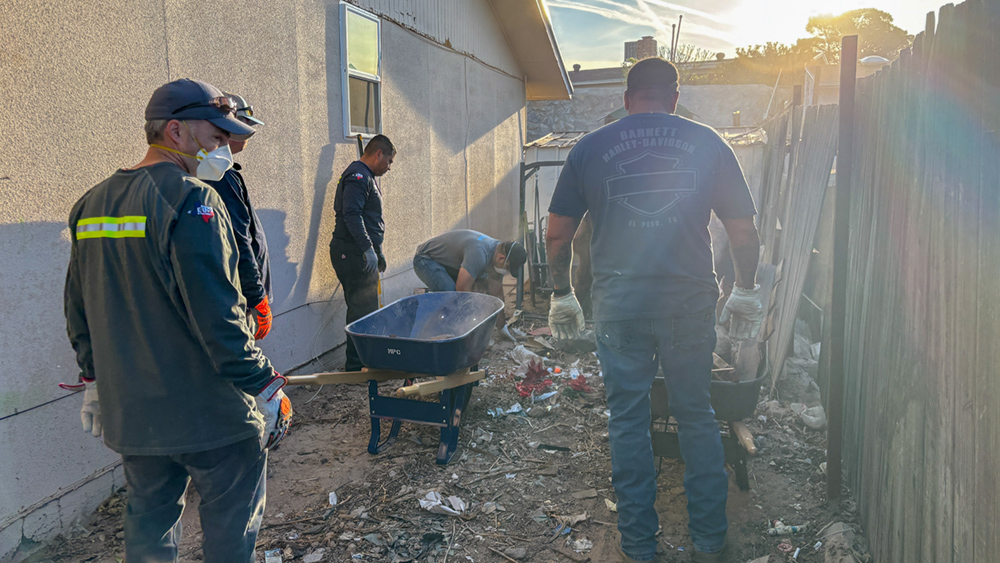 Several people use wheelbarrows to collect debris on the ground. 