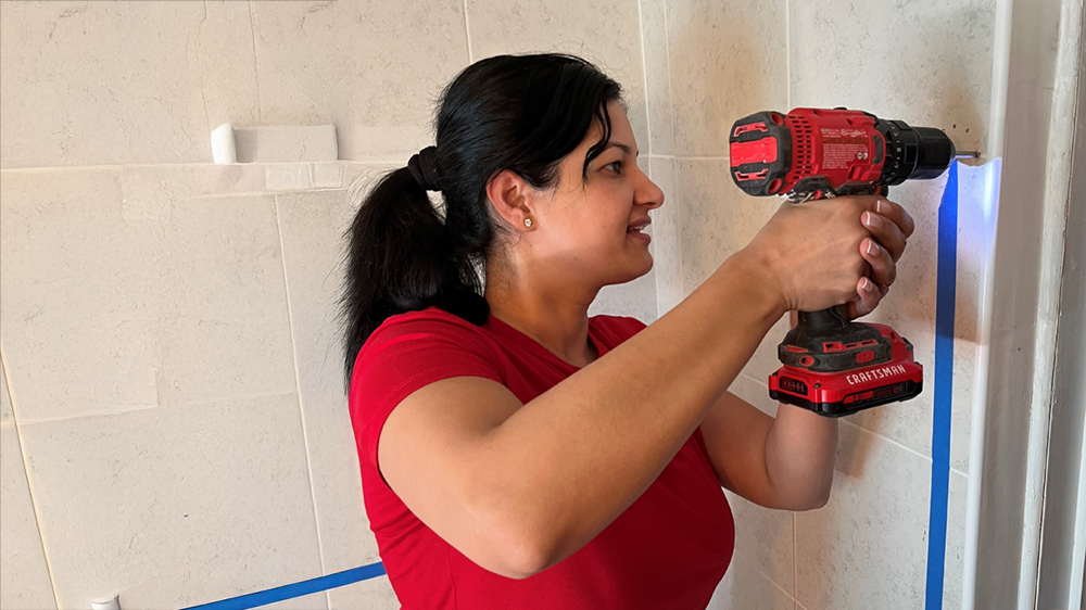  A woman using a cordless drill to create a hole in a tiled wall. 