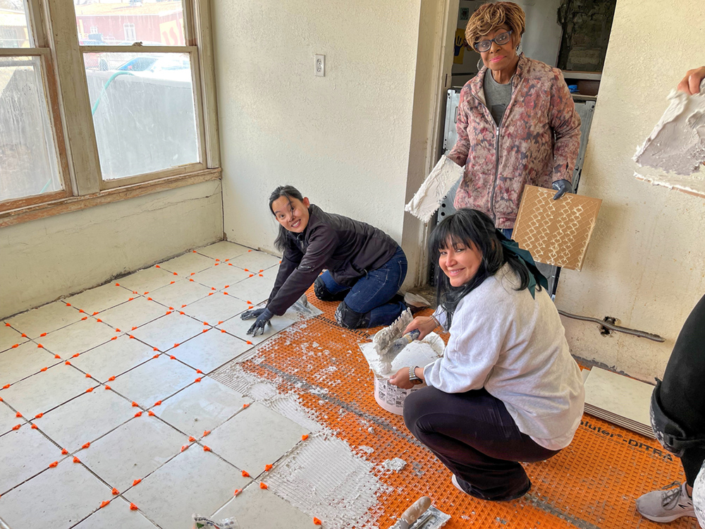 People standing and kneeling while installing floor tiles. 