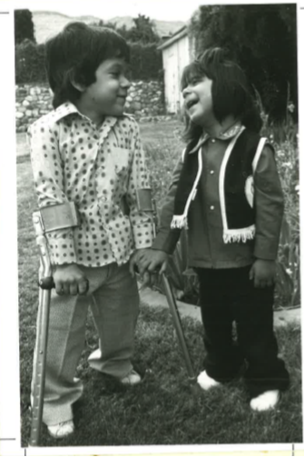 Two young children standing side by side and looking at each other. 