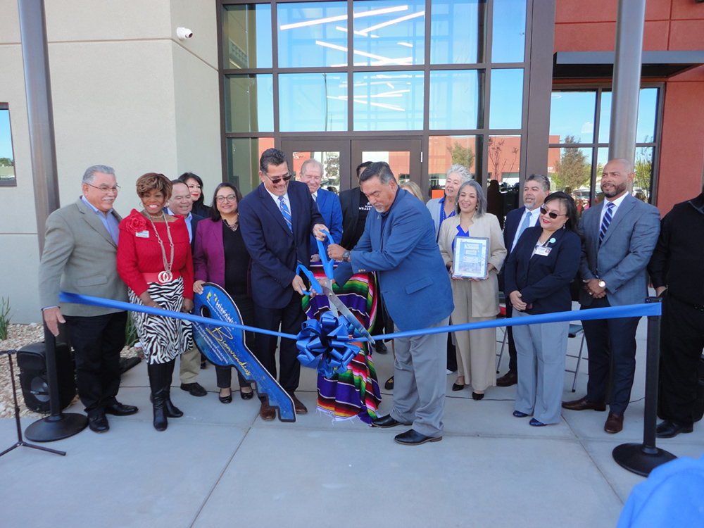 A large group of people watch as two men cut a long ribbon.