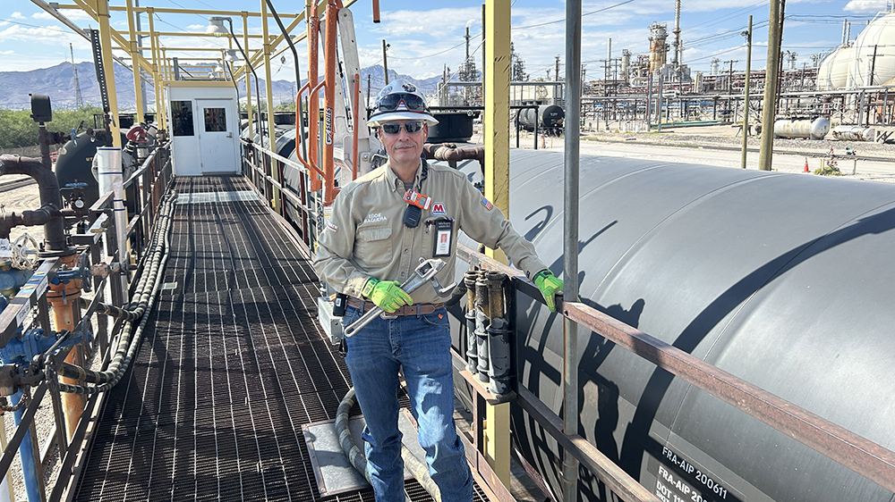 Man stands on a walkway at a loading rack next to a railcar. 