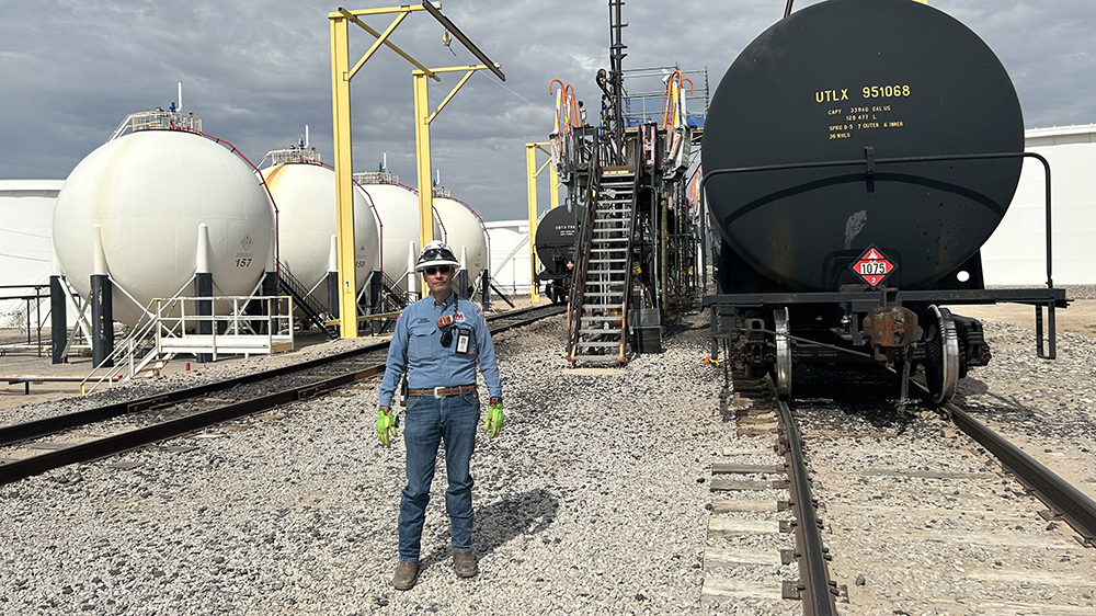 Man wearing safety gear stands in a railyard at a refinery.